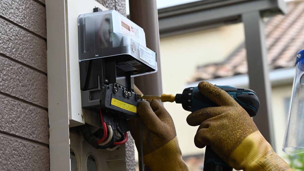 Mains gantées vissant le bornier d'un compteur électrique